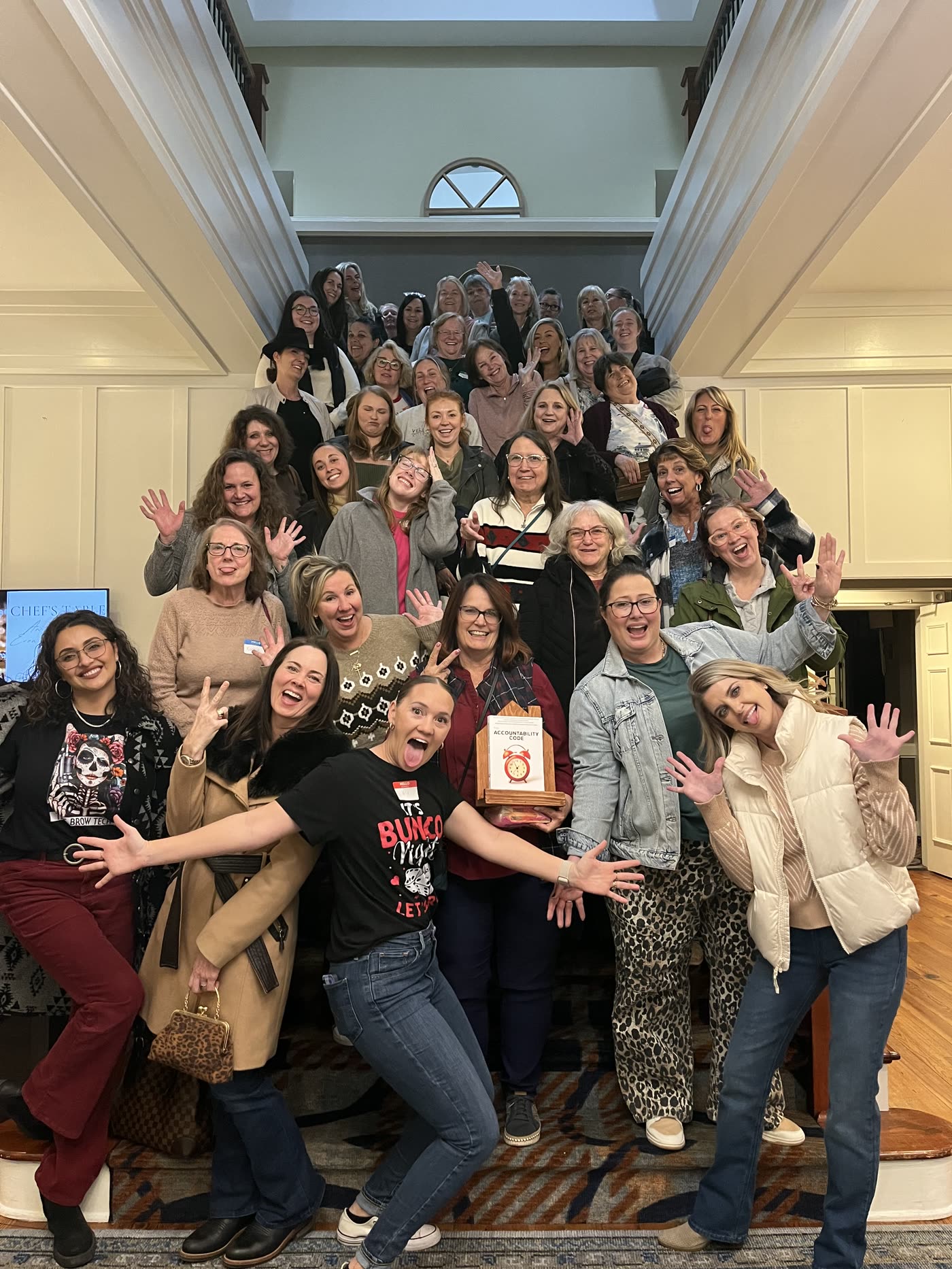 A big group of women laughing on a staircase at a Bunco with Marci night